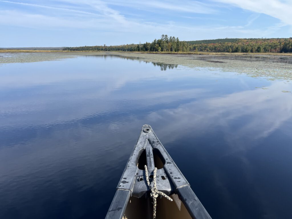 Canoe gliding across a calm lake in Maine with clear blue sky and forested shoreline in the distance